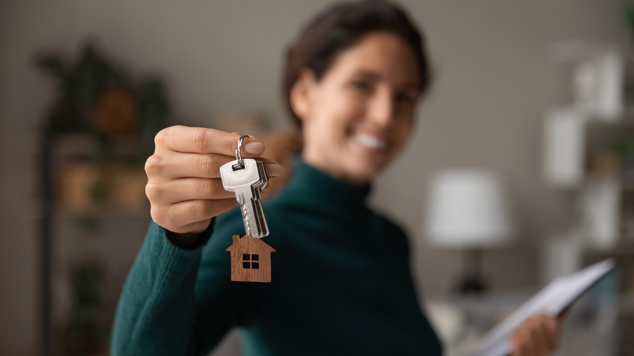 Close up focus on keys, smiling woman realtor selling apartment, offering to client, showing at camera, holding documents, contract, making purchasing deal, real estate agent, mortgage or rent